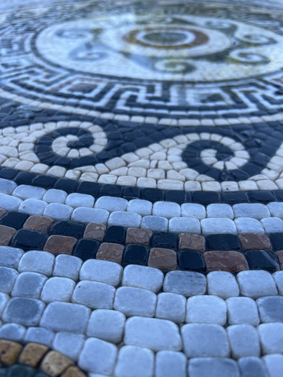 Close-up of a blue and white geometric mosaic medallion and individual stone pieces.